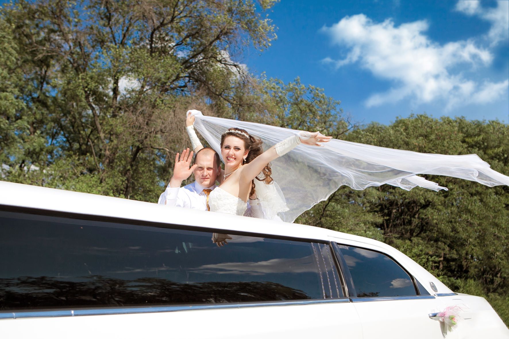 Bride and groom standing in Limo waving